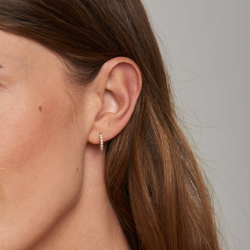 Our diamond gold huggie earrings in 14 karat gold feature pineapple charms with a handset green emerald stone. A beautiful diamond earring that feels light and comfortable on the ear. All day - all night. Take of the charm and wear the timeless diamond huggies on its own! 